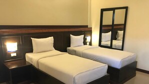 A hotel room with two single beds, a nightstand with a lamp, and a large mirror on the wall.