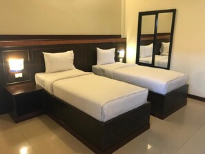 A hotel room with two single beds, a nightstand with a lamp, and a large mirror on the wall.