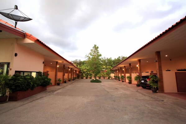 A hotel courtyard with a central pathway, potted plants, and a car parked on the right.