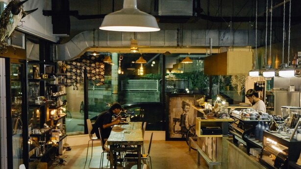 A restaurant with a long counter, tables, and chairs. There are hanging lights and a person working at the counter. - AIEN Coffee and hostel (Chatan)