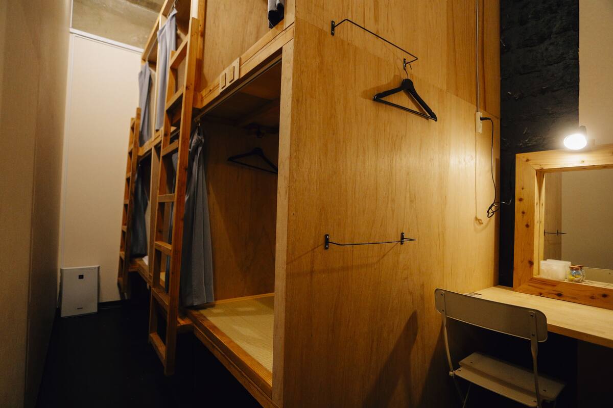 Un lit superposé en bois avec un bureau et une chaise, un portant à vêtements et un miroir.