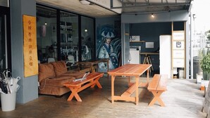 An interior with a wooden table and benches, a sofa, and a wall with a sign. - AIEN Coffee and hostel (Chatan)