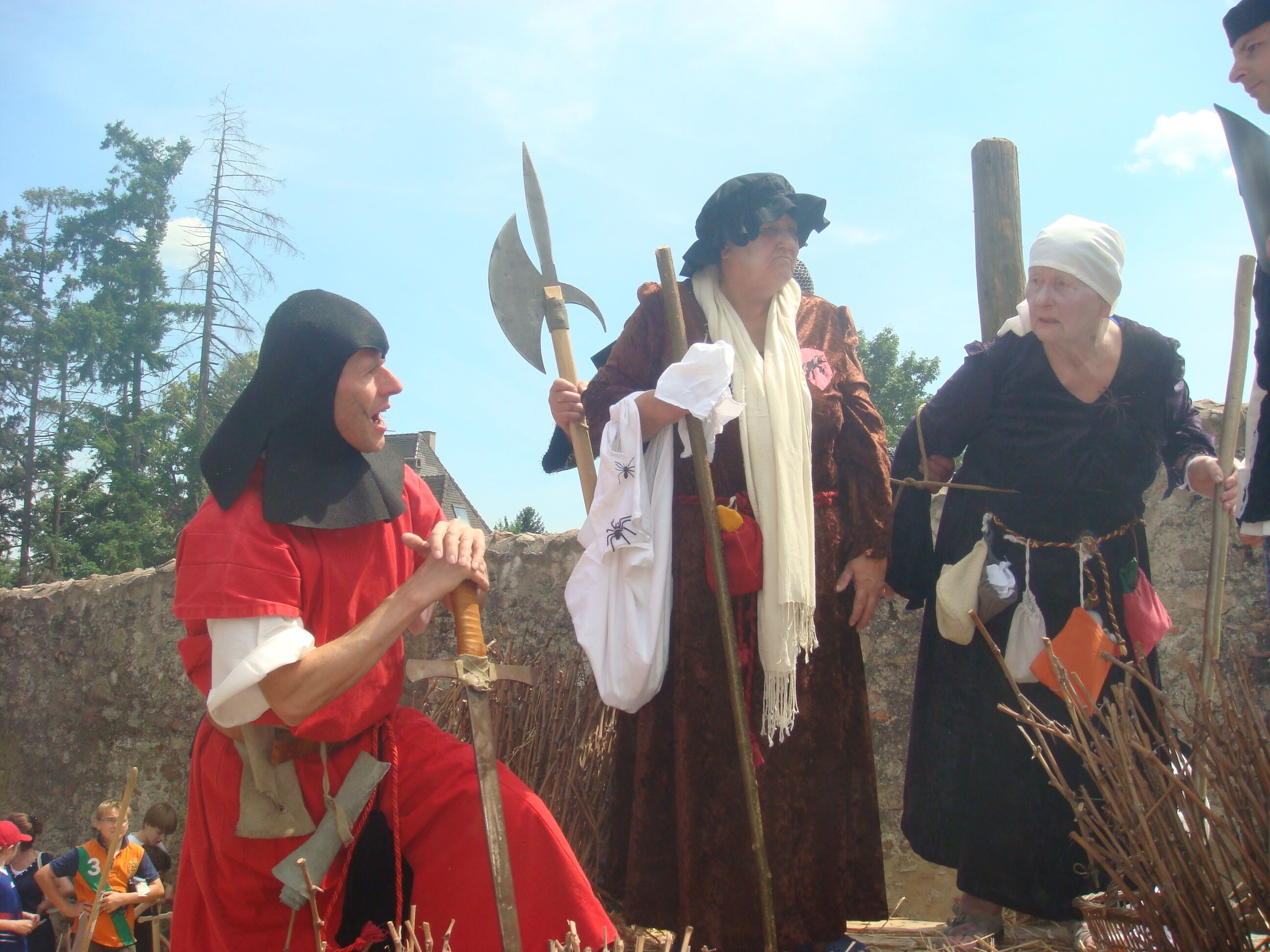 Un gruppo di persone in costumi d'epoca, che tengono in mano oggetti di scena come una spada e un'ascia, in piedi di fronte a un muro di pietra.