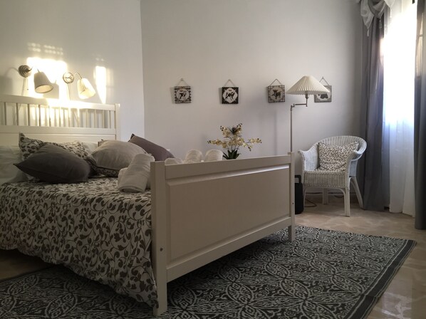 A neatly arranged bedroom with a bed, pillows, a chair, a floor lamp, and wall decorations. - Casa Albéitar, easy Parking, Wifi, Ronda (Ronda)