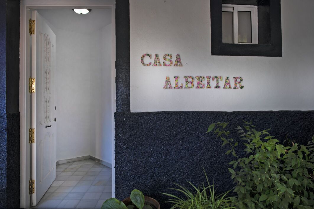A hallway with a door, a wall with the text "CASA ALBEITAR," and some potted plants.