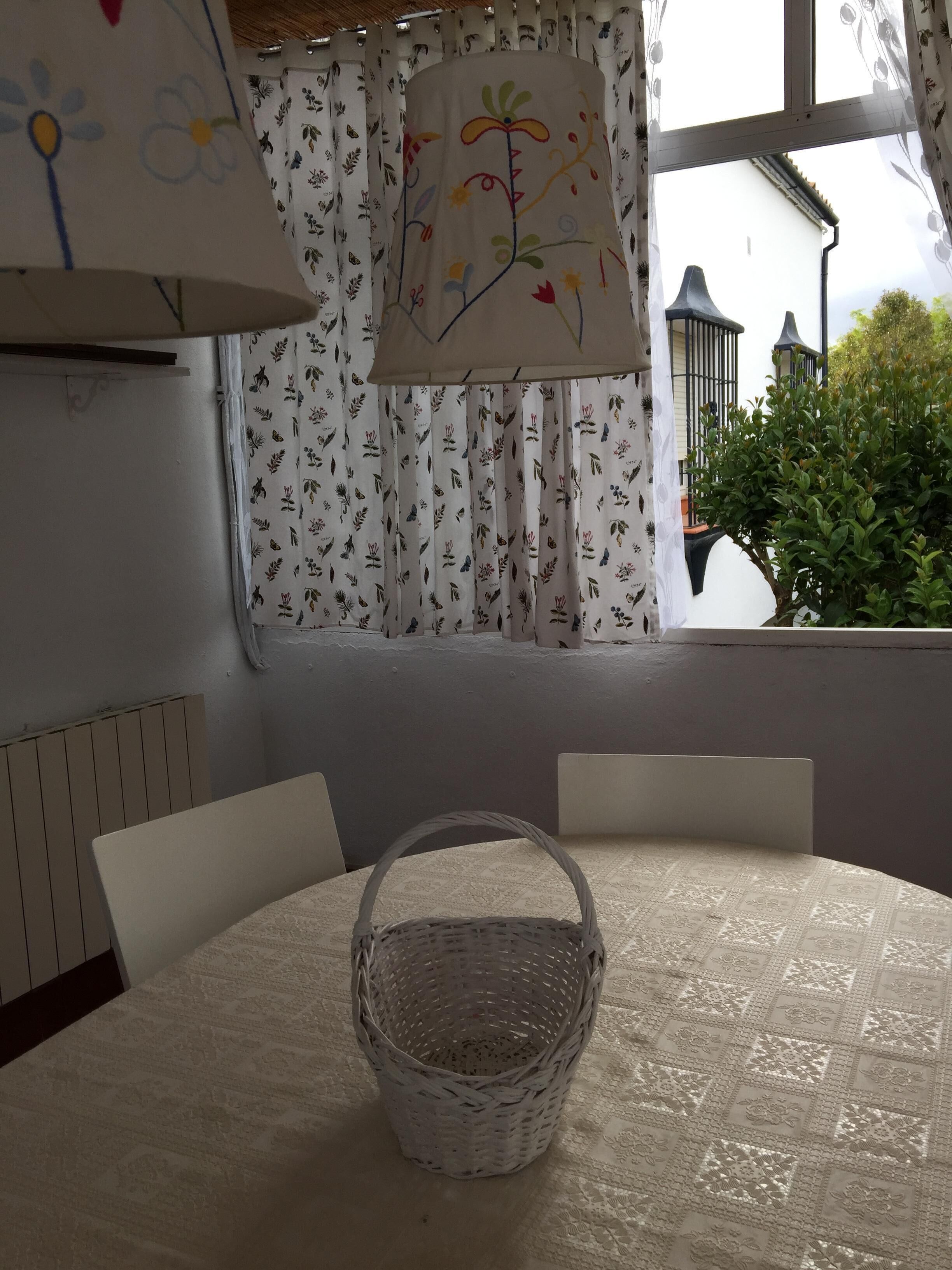 Una stanza con un tavolo rotondo, un cesto in vimini e una finestra con tende decorate.