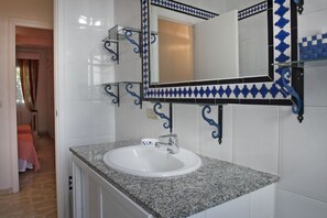 A bathroom with a white sink, a mirror with blue and black decorative tiles, and a glass shelf. - Casa Albéitar, easy Parking, Wifi, Ronda (Ronda)