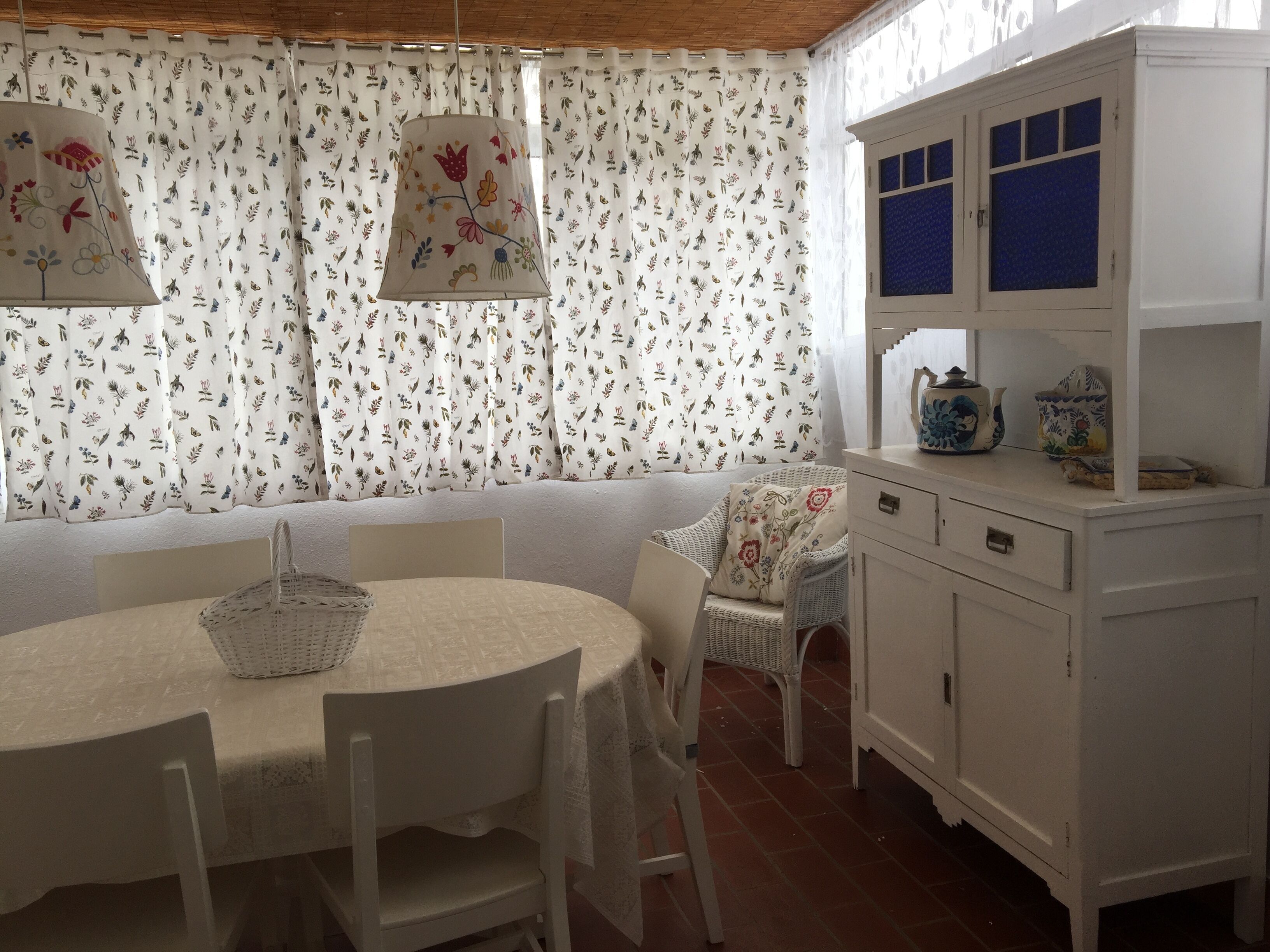 Un comedor con una mesa redonda, sillas blancas, un banco y un armario con ventanas de tono azulado.