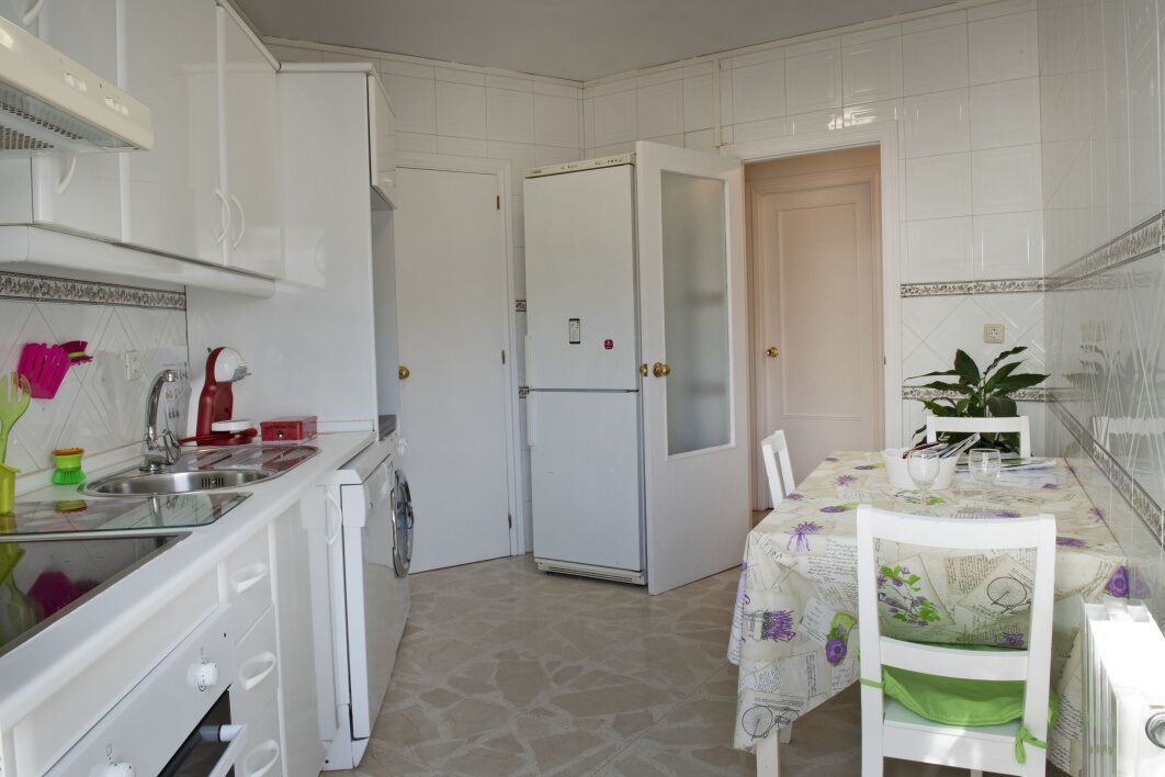 Una cocina compacta con armarios blancos, un refrigerador, un lavamanos y un comedor con mesa y sillas.