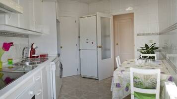 Una cocina compacta con armarios blancos, un refrigerador, un lavamanos y un comedor con mesa y sillas.