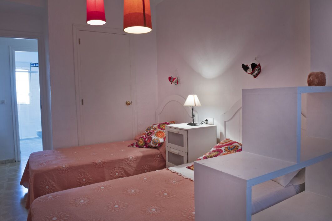 Un dormitorio con dos camas, una mesita de noche con lámpara y un aparador.