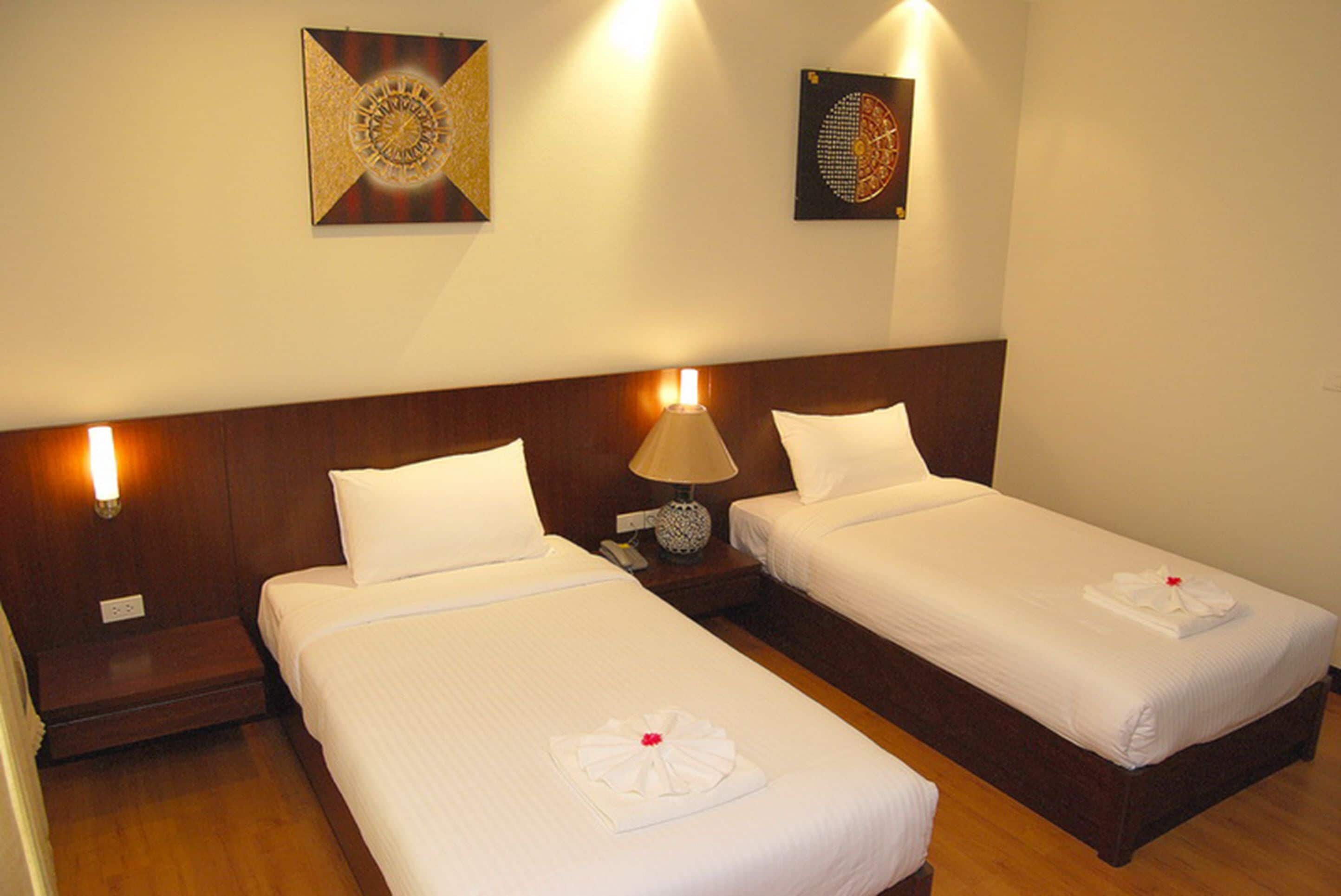 A hotel room with two single beds, each with a white bedspread and pillows, a bedside lamp, and a small table with a phone.