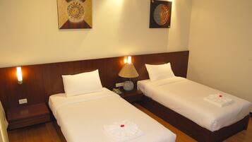 A hotel room with two single beds, each with a white bedspread and pillows, a bedside lamp, and a small table with a phone.