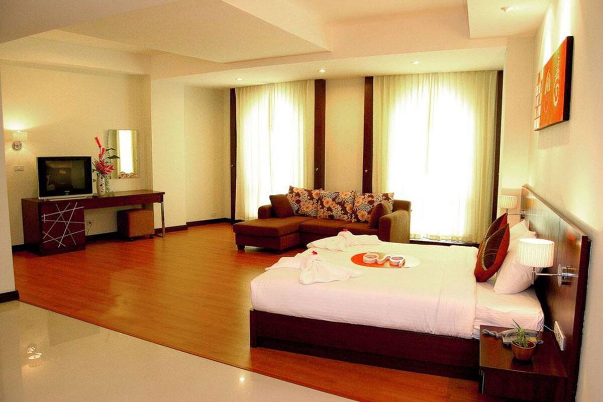 A hotel room with a bed, a sofa, a desk with a TV, and a large window with curtains.