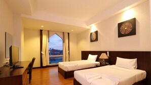 A hotel room with two beds, a desk, and a large window with curtains. - Grand Southern Hotel (Thung Song)