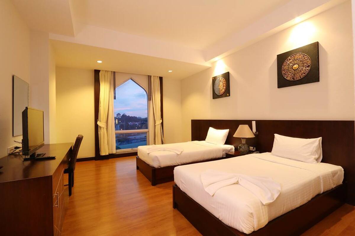 A hotel room with two beds, a desk, and a large window with curtains.