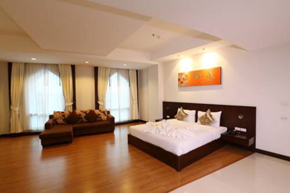 A modern hotel room with a large bed, a sofa, and a painting on the wall.