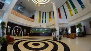 A spacious lobby with a central circular black and white floor design, a chandelier, and a reception desk with a scenic mural. - Grand Southern Hotel (Thung Song)