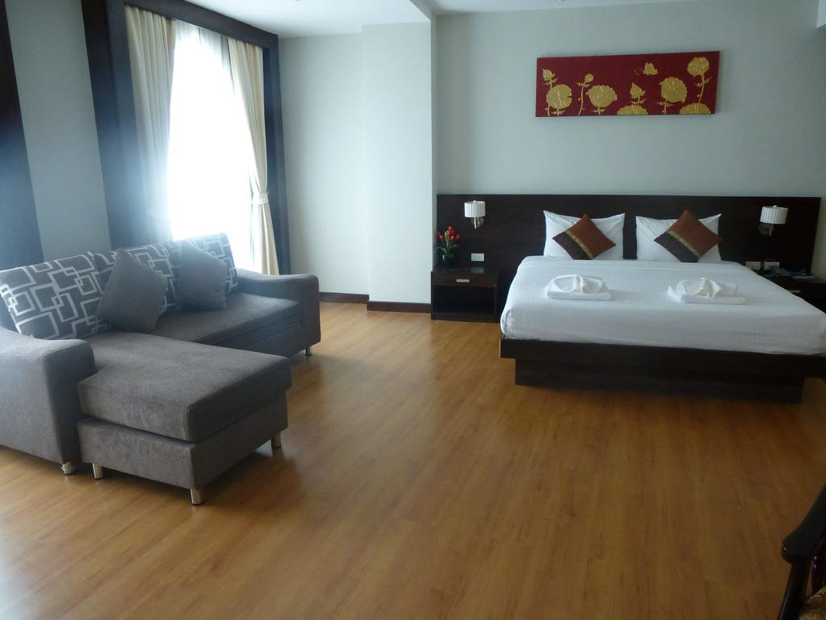 A hotel room with a sofa, a bed with pillows, a nightstand, and a wall art piece.