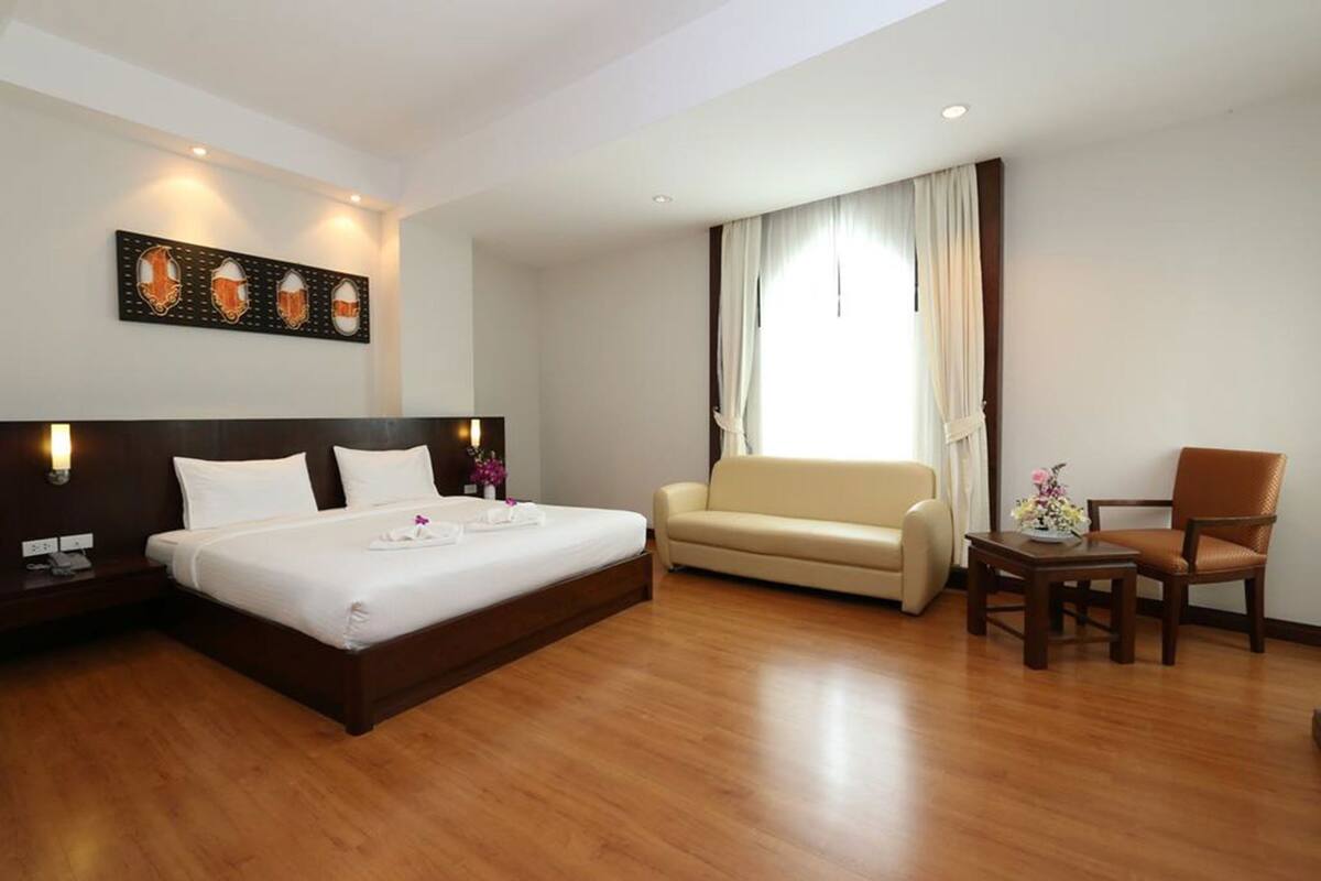 A hotel room with a large bed, a sofa, a chair, and a small table.