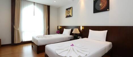 A hotel room with two beds, a large window with curtains, a wall-mounted artwork, and a nightstand with a lamp.