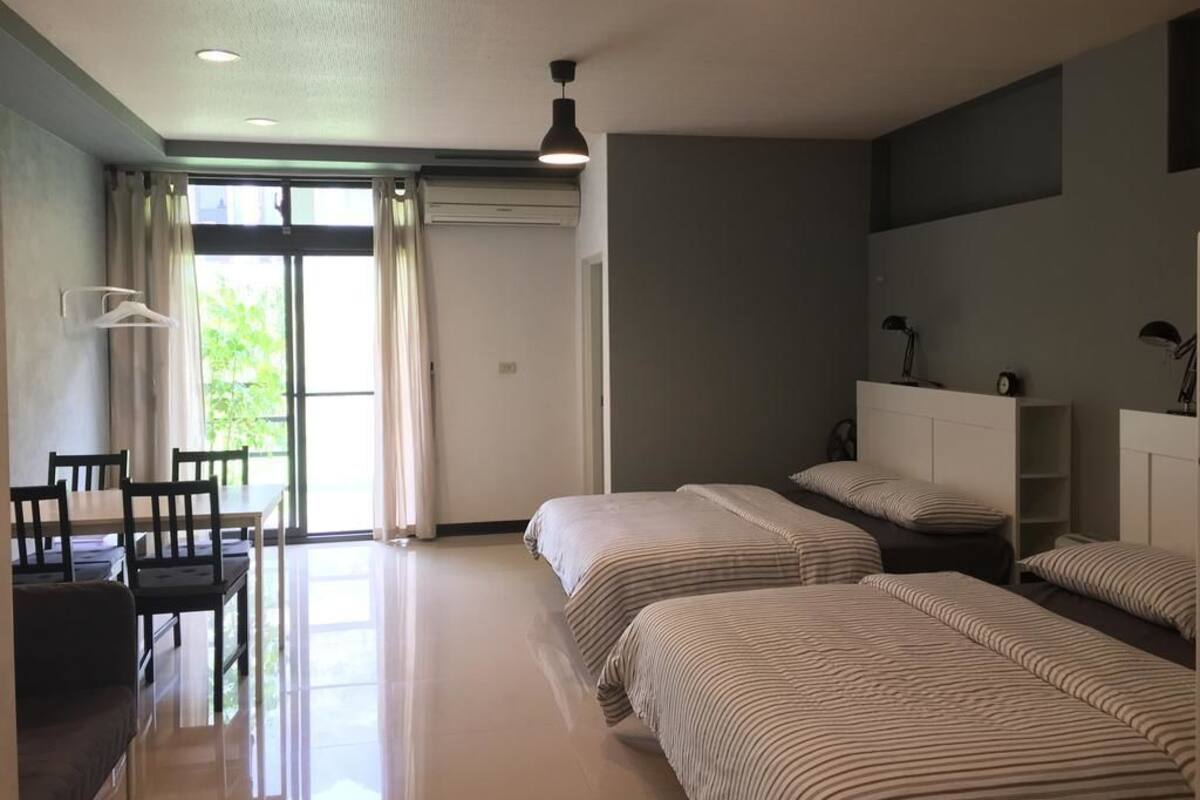 Una habitación de hotel con zona de comedor, dos camas, un armario y una ventana con cortinas.