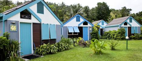 A row of small, blue and white cottages with a flat roof, surrounded by lush greenery.