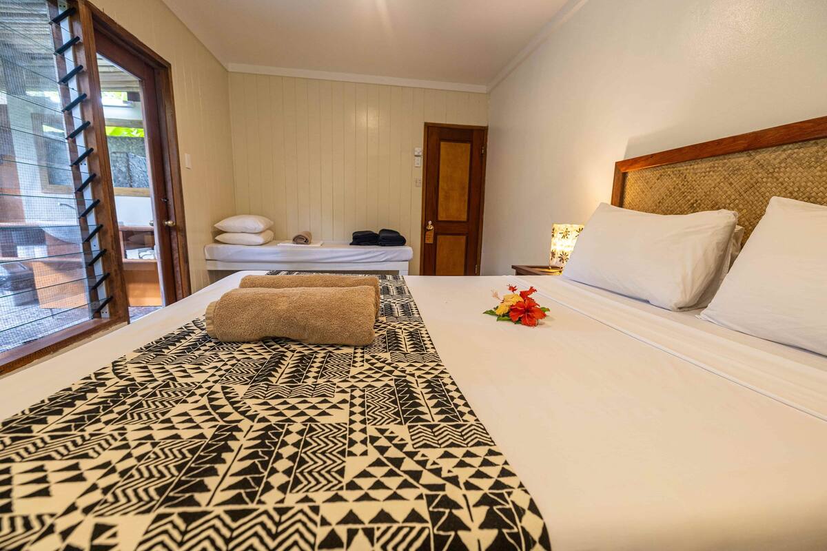 A hotel room with a bed, a small table with a lamp, a door, and a window with a view.