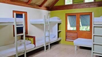 A dormitory room with bunk beds, wooden beams, and a window with shutters.