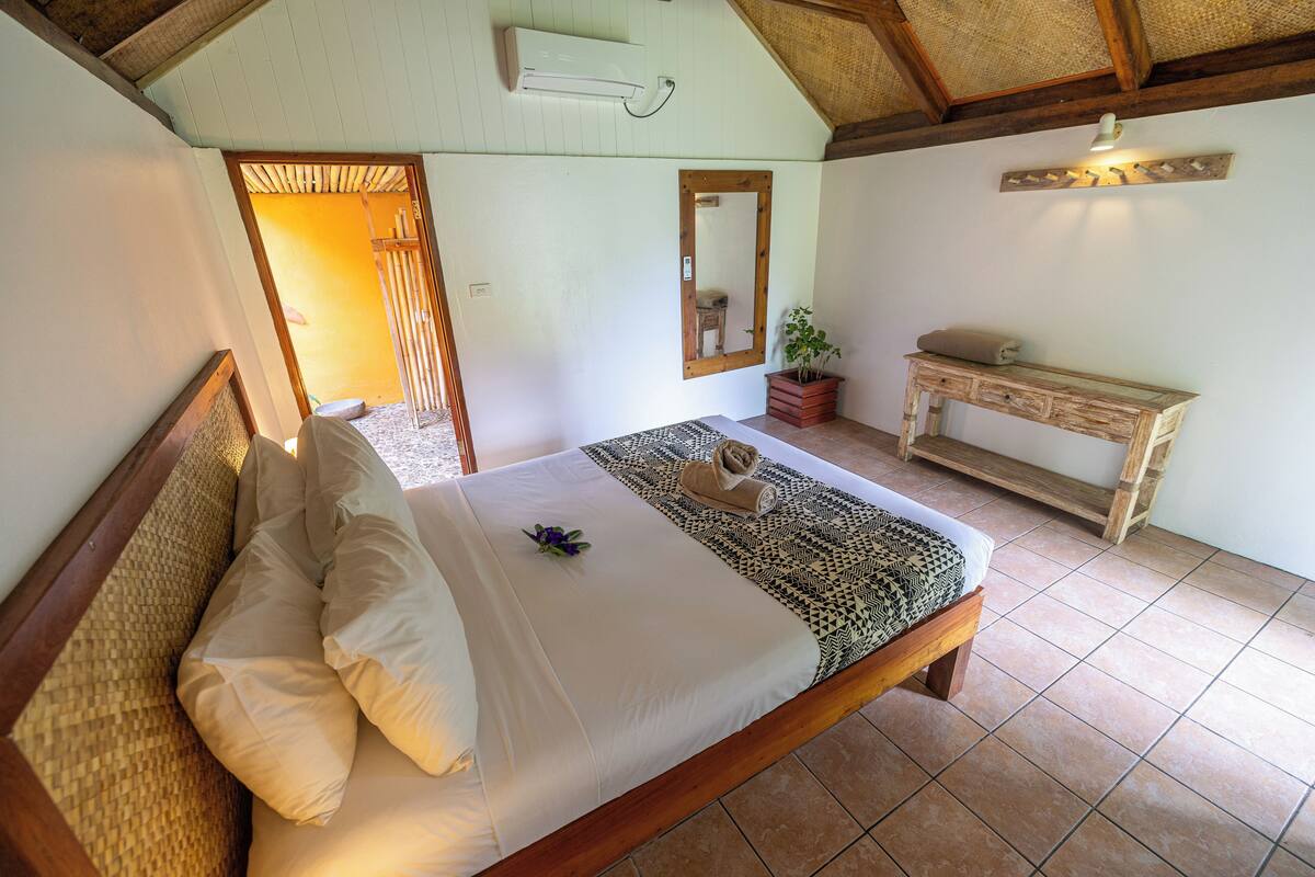 A bedroom with a bed, a bedside table, a mirror, and a potted plant.