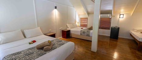 Habitación de hotel con techo alto, dos camas, piso de madera y un pequeño rincón de descanso.