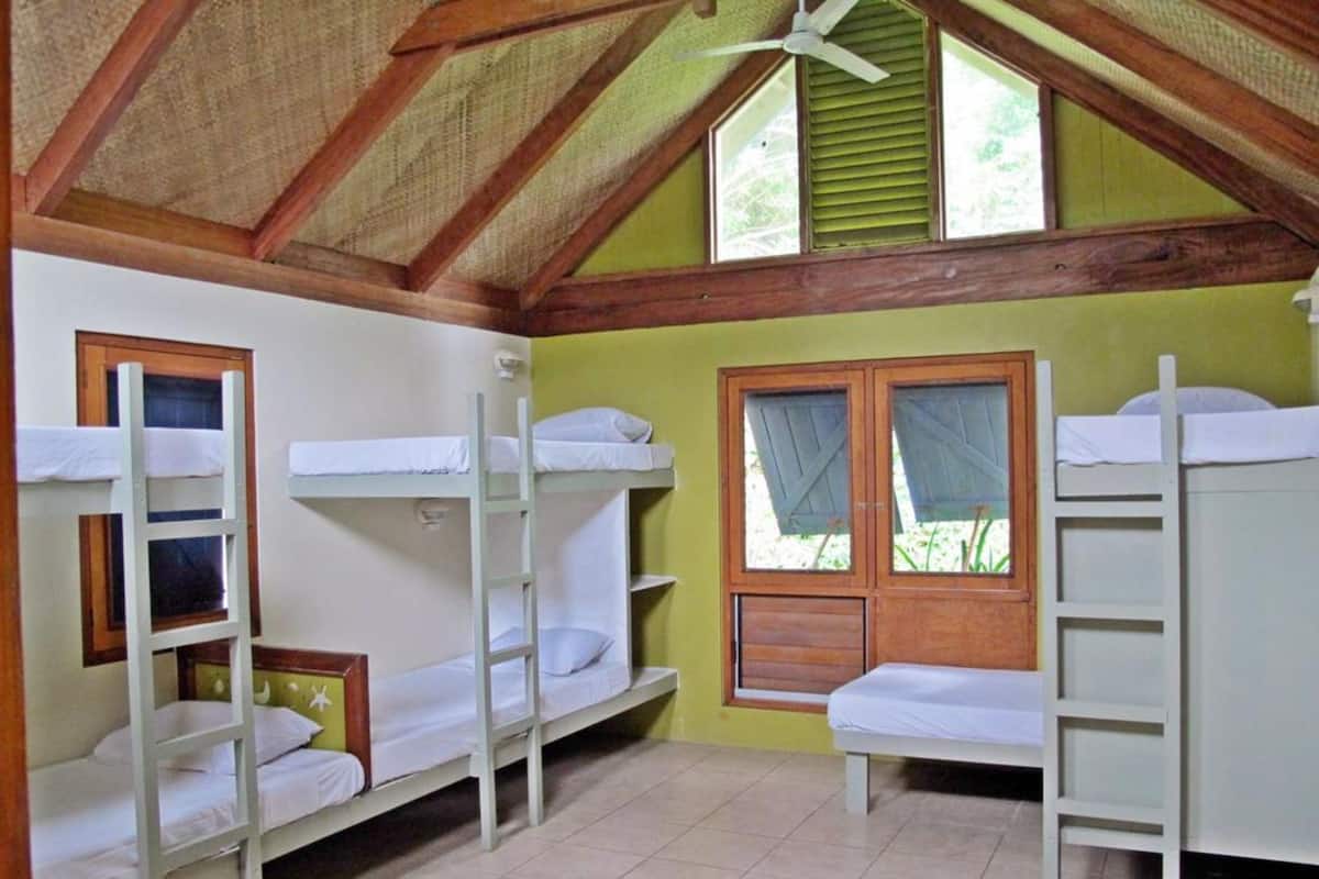 A dormitory room with bunk beds, a ceiling fan, and windows with shutters.