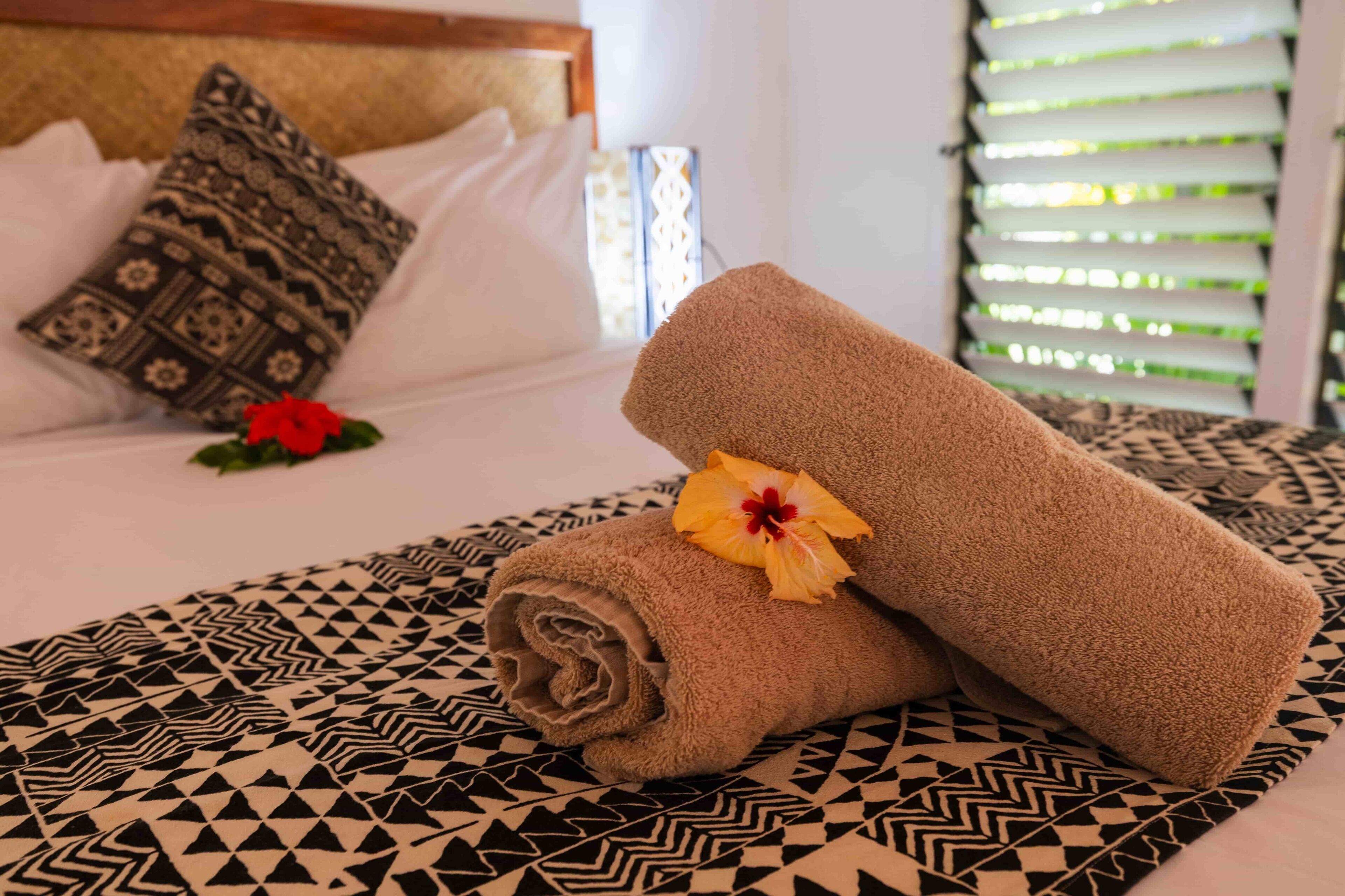 Ein ordentlich gemachtes Bett mit gemusterten Kissen und einem Blumen-Dekorierten Handtuch.