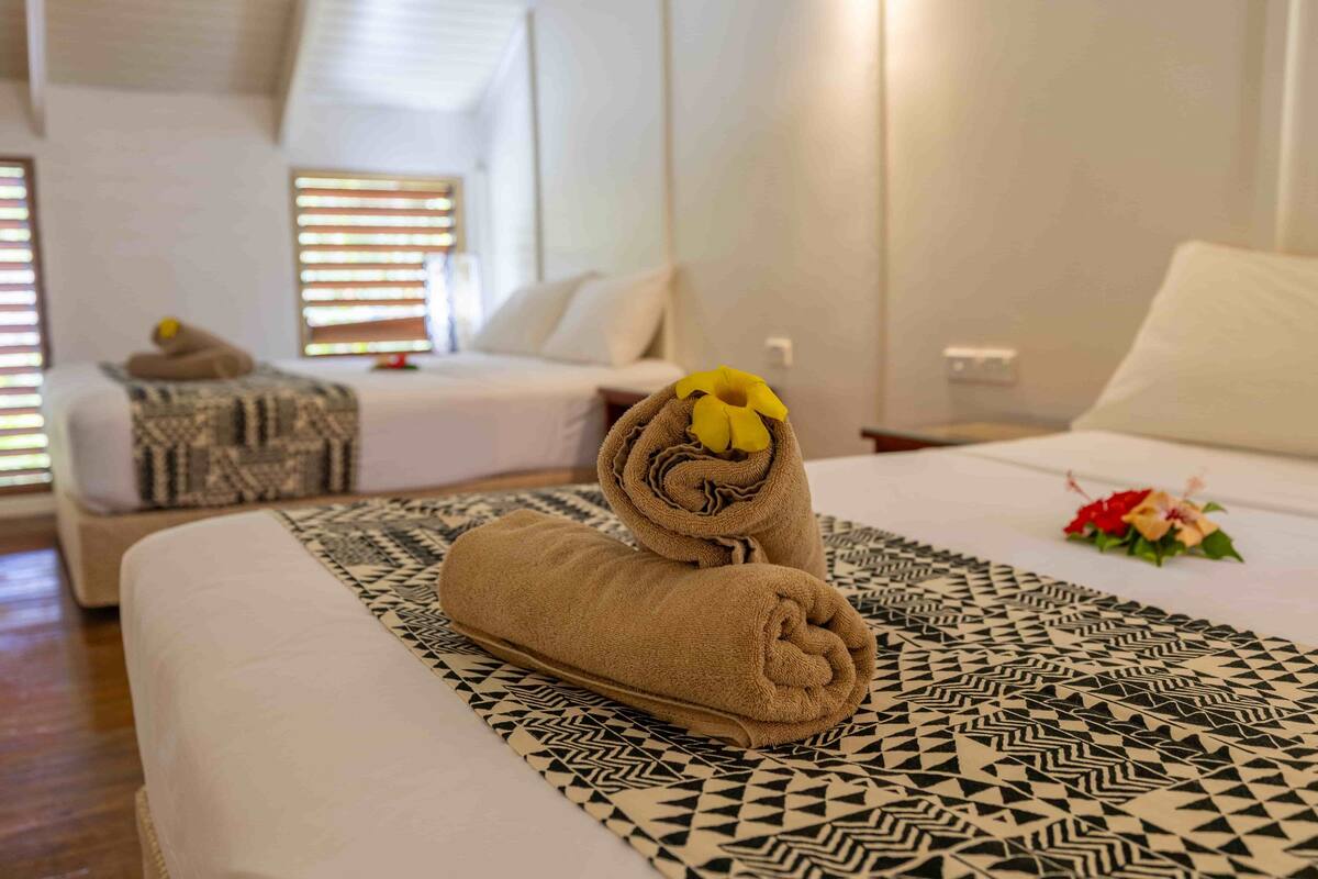 A hotel room with a neatly made bed, a patterned throw, and a small table with a decorative item.