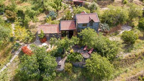 A house with a red-tiled roof surrounded by lush greenery and a patio area with outdoor seating.