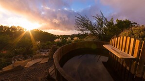 A wooden hot tub surrounded by a garden with rocks and plants.