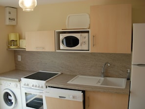 Une cuisine compacte équipée d’un four à micro-ondes, d’une cuisinière, d’un évier et d’un lave-linge.