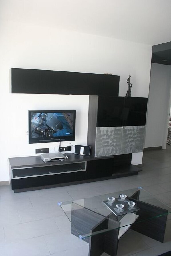Una sala de estar moderna con un televisor de pantalla plana, una mesa de centro de vidrio y un mueble blanco y negro de diseño minimalista.