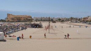 Una playa con gente, sombrillas y un edificio al fondo.