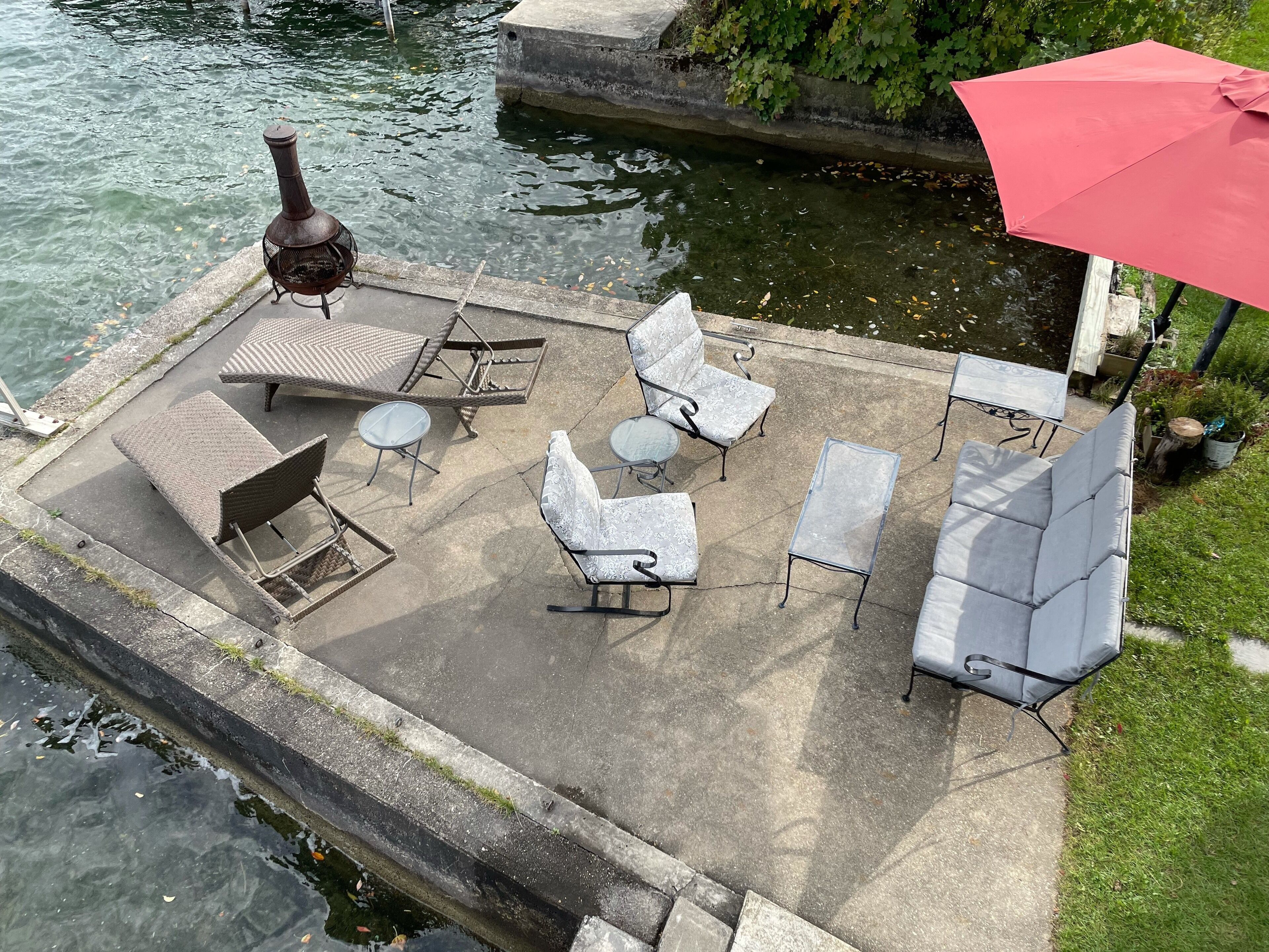A patio with outdoor furniture, a red umbrella, and a view of the water.