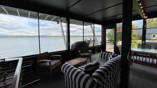 L'intérieur d'un bateau, avec une grande fenêtre donnant sur un lac, un coin salon avec des sièges rembourrés et une table.