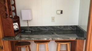 Une cuisine dotée d’un plan de travail en marbre foncé, de tabourets en bois et d’un luminaire fixé au mur.
