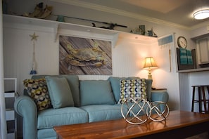 A living room with a light blue sofa, patterned cushions, a wooden coffee table, decorative items, and a wall-mounted lamp.