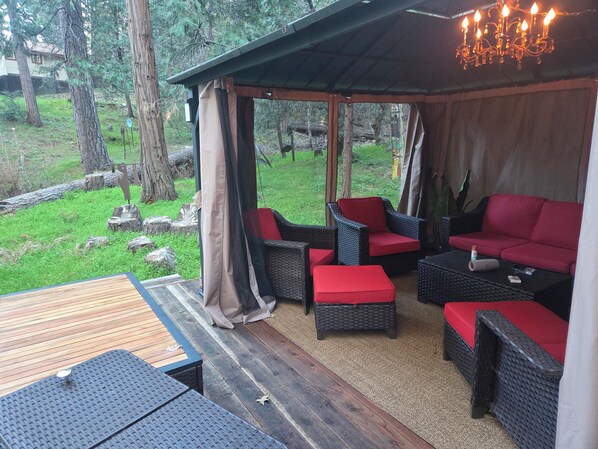 An outdoor seating area with wicker furniture and red cushions, a wooden deck, and a covered section with a chandelier.