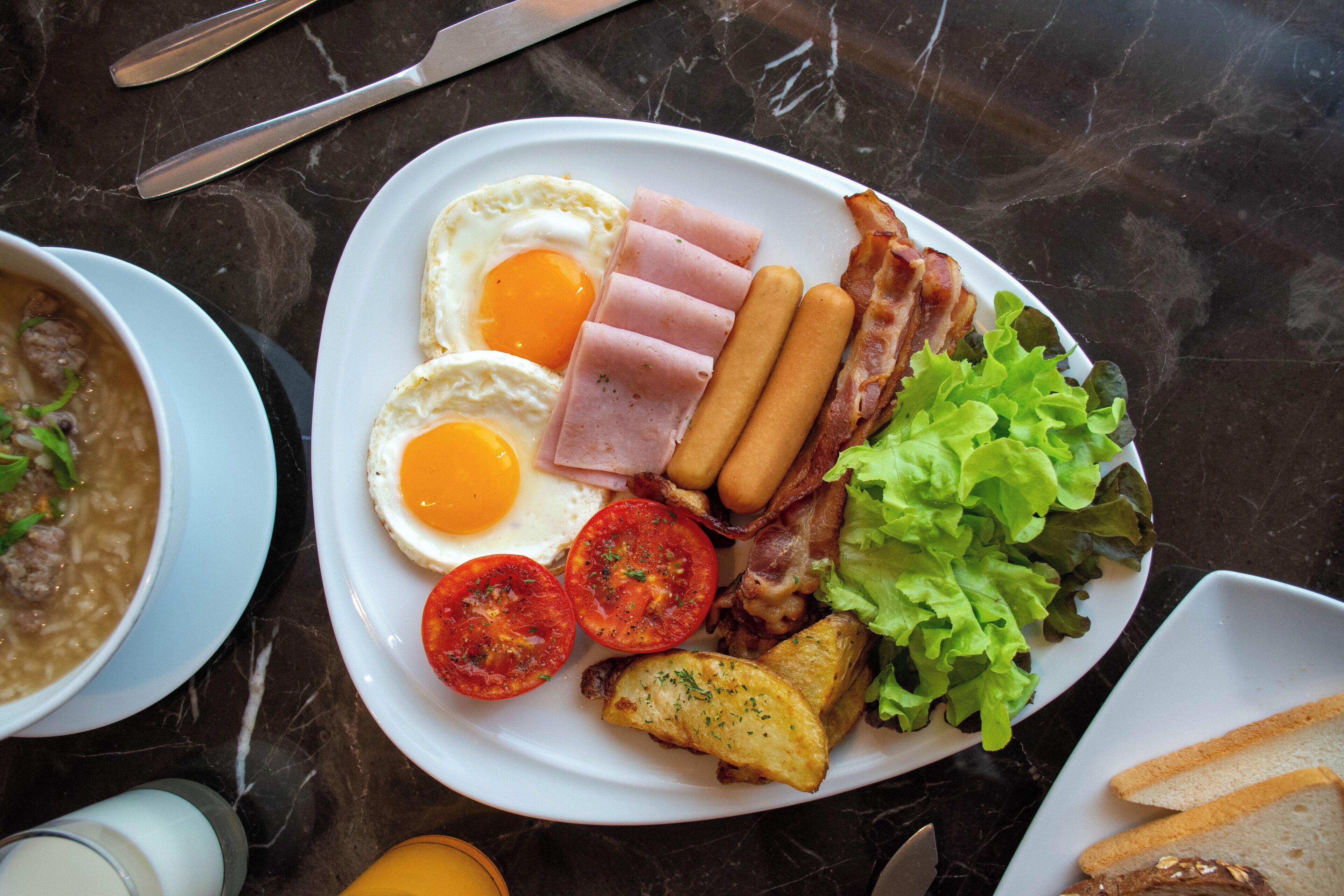 A breakfast plate with eggs, ham, bacon, sausages, tomatoes, lettuce, and toast.