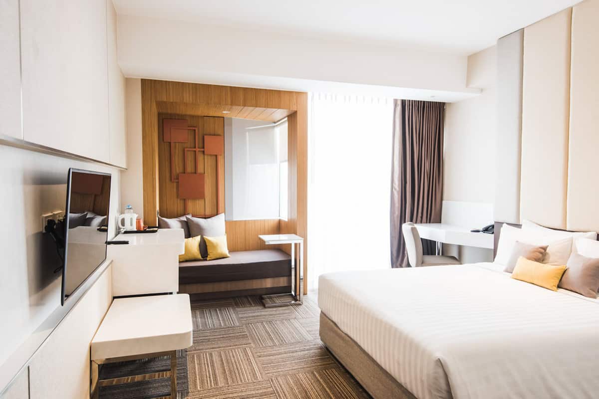 A modern hotel room with a bed, a desk, a sofa, and a TV.