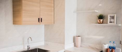 Una cocina moderna con un lavamanos, armarios de madera, salpicadero de mármol y una encimera con una bandeja que contiene un rollo de toallas de papel, una planta pequeña y dos botellas.