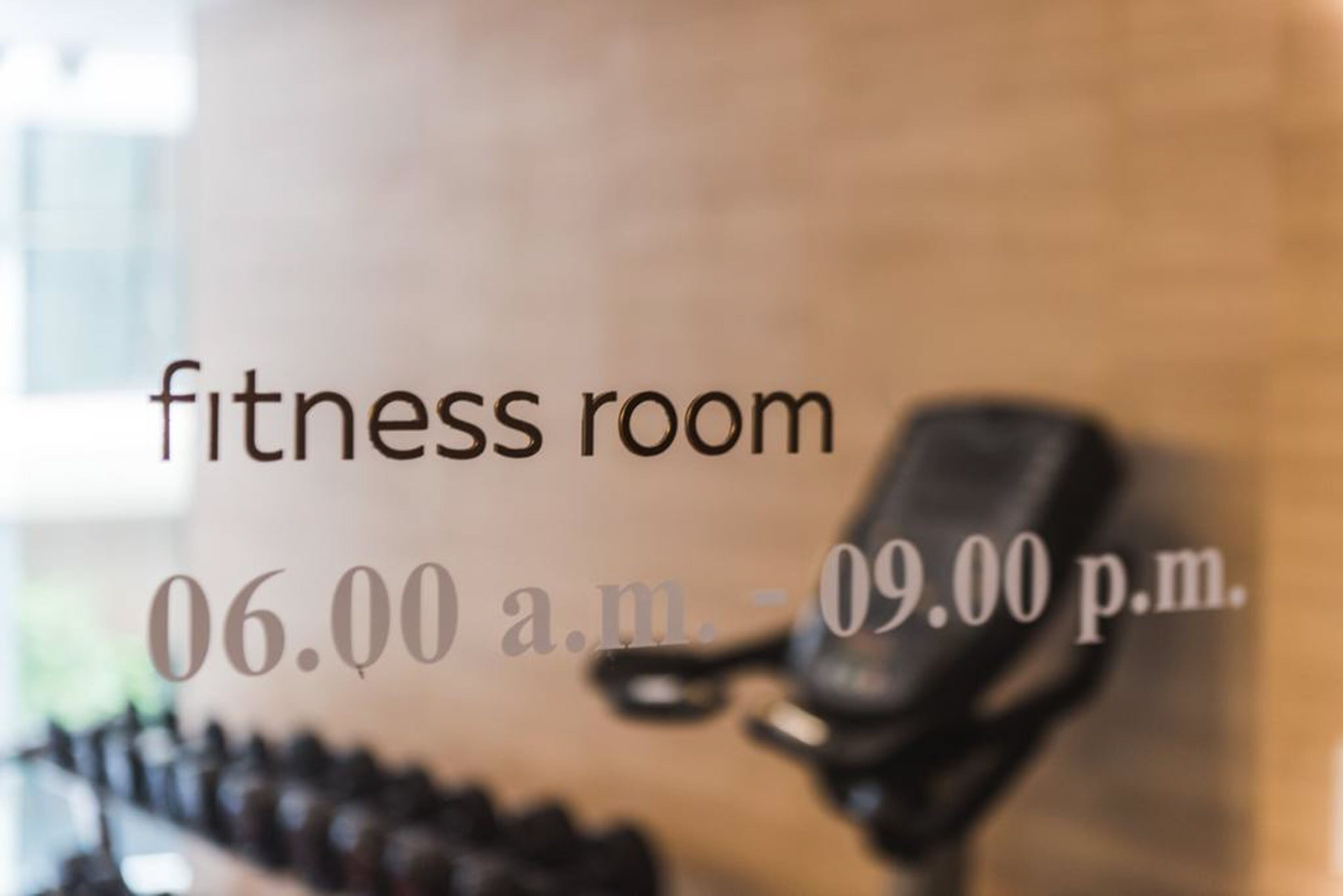 Een fitnessruimte met een aan de muur bevestigd trainingsapparaat en een bordje met de openingstijden van 6:00 uur 's ochtends tot 21:00 uur 's avonds.