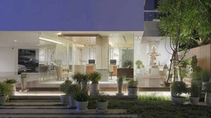 En moderne hotelindgang med en glasfacade, udendørs siddeområde og plantekasser.