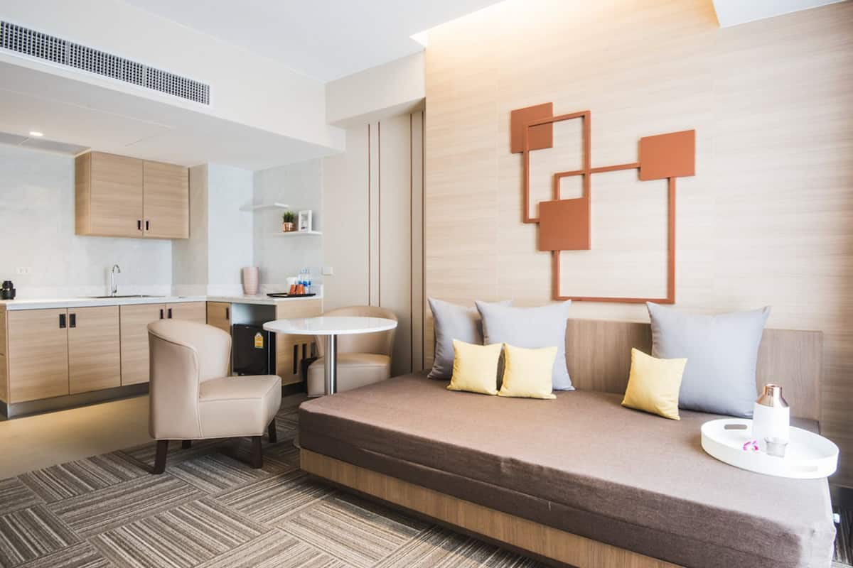 A modern hotel room with a sofa bed, a small round table, a chair, and a kitchenette.